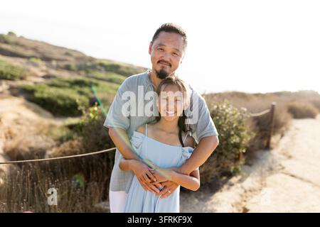 Père asiatique heureux embrassant sa fille en plein air par une journée ensoleillée Banque D'Images