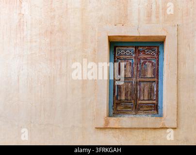 Fenêtre en bois rustique patiné sur un mur en plâtre ocre texturé à Marrakech, Maroc. Détail architectural vintage authentique avec espace de copie. Banque D'Images