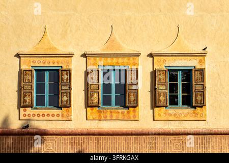 Vue frontale symétrique de fenêtres ornées rustiques sur une façade jaune à Marrakech, capturant la culture authentique et une ambiance chaude et ensoleillée. Banque D'Images