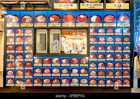 Des images de kaisendon garni de thon, de roe de saumon, d'oursin et de crevettes, avec des prix en yens, recouvrent la façade d'un restaurant japonais le soir à Tokyo Banque D'Images