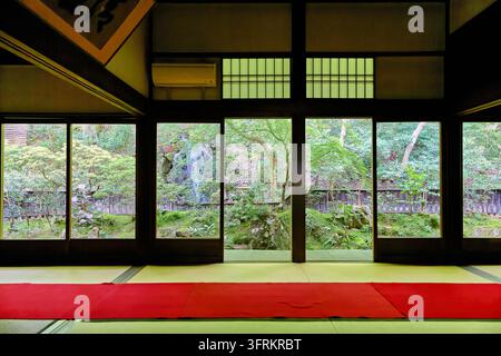 Tapis en feutre rouge sur tatami dans un intérieur de temple traditionnel, avec des fenêtres ouvertes donnant sur un jardin printanier avec lanterne en pierre et érables. Banque D'Images