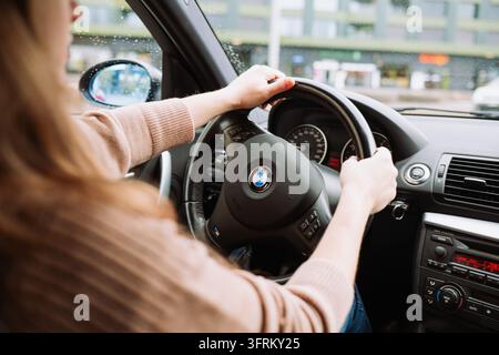 Urdorf, Zurich, Suisse, 10 octobre 2026. Vue par-dessus l'épaule d'une conductrice tenant le volant d'une voiture BMW tout en conduisant sur une voie Banque D'Images