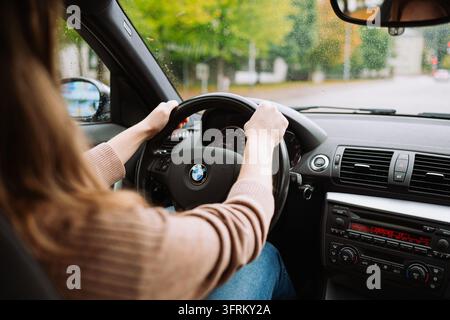 Urdorf, Zurich, Suisse, 10 octobre 2026. Vue par-dessus l'épaule d'une femme tenant le volant et conduisant une voiture BMW sur une route mouillée sous la pluie Banque D'Images