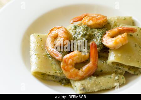 Vue en hauteur de paccheri au pesto de câpres et aux crevettes dans un bol blanc, garni de quatre crevettes, lumière naturelle douce Banque D'Images