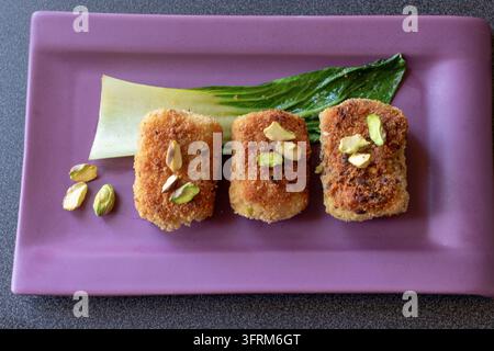 Vue en hauteur de paccheri frits farcis à la ricotta, au prosciutto et aux pistaches sur une assiette rectangulaire violette, lumière naturelle douce Banque D'Images