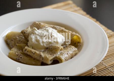 Vue en contre-plongé de paccheri au pesto de radicchio et stracciatella dans un bol blanc sur un tapis en bambou, lumière naturelle douce Banque D'Images