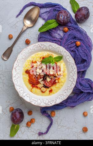 Porridge de millet avec des prunes caramélisées, des noisettes, du cinnamon et un brin de menthe dans un bol sur un fond texturé fissuré. Plat végétalien sain. Vue de dessus Banque D'Images
