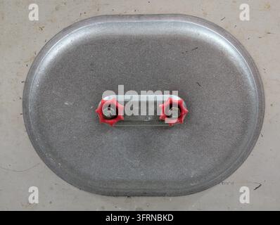 Couvercle de trappe d'accès en métal avec deux boutons de serrage en forme d'étoile rouges montés sur une surface en béton plat, vue centrée par-dessus montrant une galvanisation texturée Banque D'Images