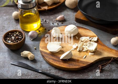 Champignons frais tranchés sur une planche à découper en bois avec de l'huile d'olive, de l'ail et du poivre noir, disposés sur une surface de cuisine rustique pour des produits biologiques de saison Banque D'Images