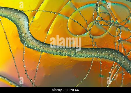 Texture liquide abstraite colorée présentant des bulles transparentes, des mèches argentées fluides et des tons jaune-orange vifs. Fond macro créatif avec Banque D'Images