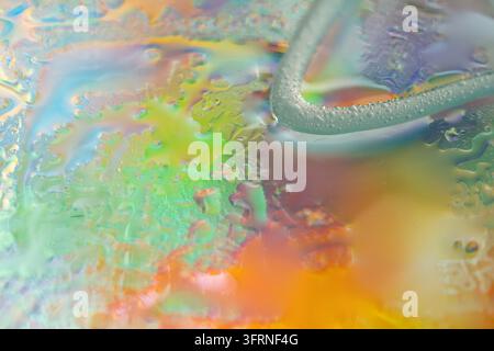 Image macro abstraite colorée de liquide irisé, de gouttelettes d'eau translucides et de teintes douces tourbillonnantes en jaune, vert, bleu, orange et violet avec Banque D'Images