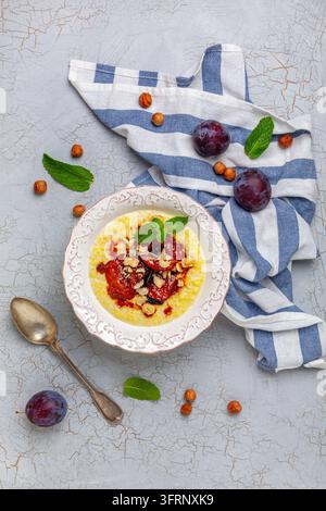 Porridge de millet avec des prunes caramélisées, des noisettes, du cinnamon et un brin de menthe dans un bol sur un fond texturé fissuré. Plat végétalien sain. Vue de dessus Banque D'Images