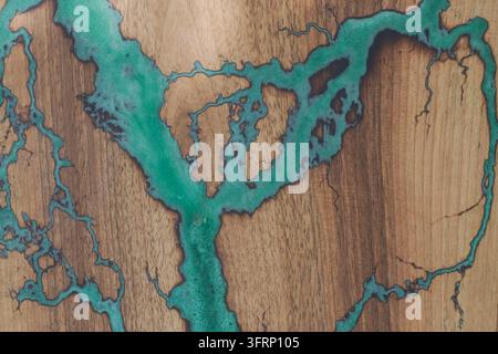 Grossissement de bois naturel avec des fissures irrégulières et des canaux ramifiés remplis de résine turquoise, créant un motif abstrait artisanal avec des éléments visib Banque D'Images