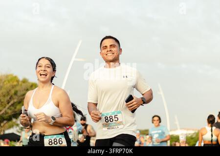 Deux coureurs souriants participent à un 5 km en course sur route en plein air, courant côte à côte tandis que d'autres participants suivent la course derrière eux. Banque D'Images
