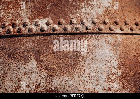 Surface métallique rouillée présentant un motif de rivets et une texture forte usée, grunge. Représentant la décrépitude et le vieillissement industriel Banque D'Images