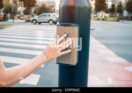 Piéton appuyant sur un bouton d'un lampadaire de feu tricolore pour un passage piéton, assurant la sécurité dans un environnement urbain Banque D'Images