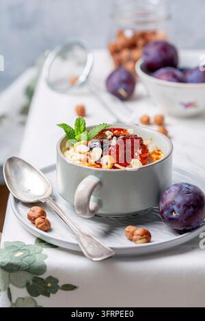 Petit-déjeuner chaud sain. Bol de porridge de millet avec des prunes caramélisées, des noisettes et du cannelle sur la table de la cuisine, mise au point sélective Banque D'Images