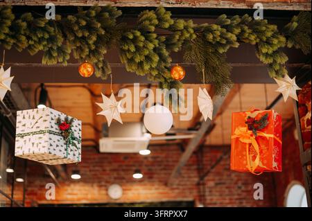 Décorations de Noël et cadeaux emballés suspendus à une guirlande de feuillage toujours vert festif dans un intérieur rustique Banque D'Images