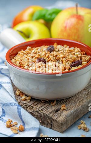 Muesli maison avec pommes et raisins secs dans un bol en céramique sur un vieux support en bois, gros plan, mise au point sélective Banque D'Images
