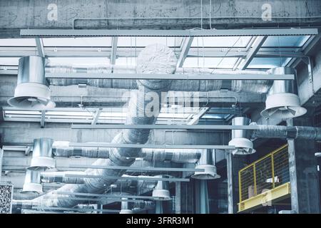 Plafond industriel avec conduits d'air exposés et ventilateurs assurant la régulation climatique et la circulation d'air dans un bâtiment industriel moderne Banque D'Images