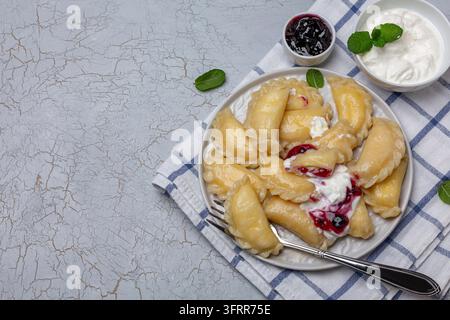 Cuisine russe et ukrainienne – boulettes de pâte avec du fromage frais servies avec une sauce aux baies et de la crème fraîche. Vue de dessus avec espace libre Banque D'Images