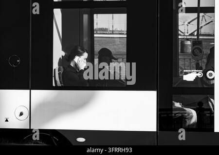 Femme au téléphone dans les transports en commun, reportage de voyage à Riga, Riga, Lettonie : Une femme parle au téléphone portable tout en étant assise dans un bus ou un tramway, encadrée par la vitre du véhicule, sur une photographie en noir et blanc. INFO : Riga, la capitale de la Lettonie, est la plus grande ville des États baltes. Alliant histoire médiévale et charme cosmopolite, elle est mondialement réputée pour son architecture Art Nouveau exceptionnelle inscrite au patrimoine mondial de l'UNESCO et sa vieille ville pavée magnifiquement préservée. Banque D'Images
