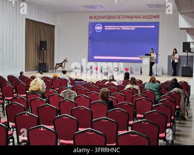 Moscou - 20 févr. 2025 : Un grand public est rassemblé dans une salle rouge avec un grand écran mural. L'écran affiche un message en russe - Académie vétérinaire internationale Banque D'Images
