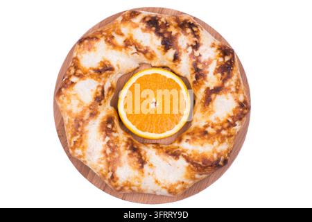 Cheesecake rond avec un morceau d'orange au centre, posé sur une planche ronde en bois, fond blanc, objet isolé Banque D'Images