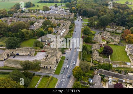 Photographie aérienne par drone de la route traversant le village de Harewood avec des bâtiments traditionnels en pierre, des rues résidentielles, des voitures garées et de grands arbres, un Banque D'Images