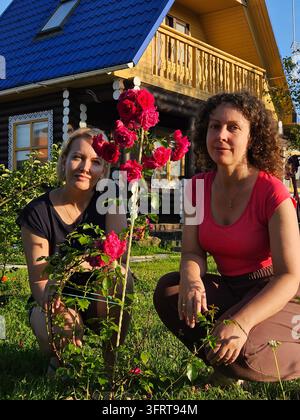 Deux femmes sont agenouillées devant un rosier. L'une d'elles porte une chemise rouge près de la datcha Banque D'Images