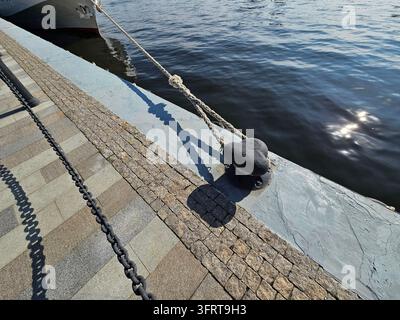 Le bateau est amarré à un quai avec une corde. La corde est attachée à un objet métallique qui ressemble à un cœur. La scène est calme et paisible, avec l'eau reflétant le ciel Banque D'Images
