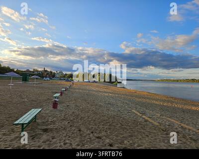 Plage avec quelques bancs et quelques voitures garées. Le ciel est bleu avec quelques nuages à Murom Banque D'Images