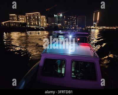Un bateau avec une lumière bleue et rouge au sommet se trouve sur une rivière la nuit. Les lumières du bateau sont vives et colorées, créant une atmosphère festive Banque D'Images