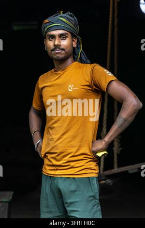 Portrait d'un travailleur confiant avec un tatouage sur l'avant-bras et des bracelets en métal portant un short vert dans un entrepôt sombre avec des cordes en arrière-plan, West Benga Banque D'Images