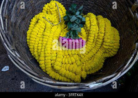 Vue de dessus de guirlandes de soucis jaunes serrées disposées dans un grand panier en osier avec un bouquet de roses violettes et des feuilles vertes au marché floral Banque D'Images