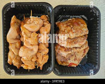 Morceaux de poulet grillés dans deux plateaux noirs. Brochettes de poulet et escalopes de poulet empilées visibles. Nourriture prête à la vente dans des contenants jetables. Aucun animal ou plante identifié dans cette image Banque D'Images