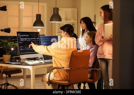 Collaboration d'une équipe de développement logiciel, des programmeuses diverses travaillant sur un projet de codage dans un bureau moderne la nuit avec écran d'ordinateur et ordinateur portable Banque D'Images