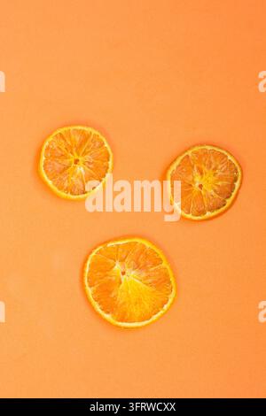 Trois tranches d'orange séchées sont disposées sur un fond orange vif dans une nature morte minimaliste vue de dessus avec un espace de copie généreux. Banque D'Images