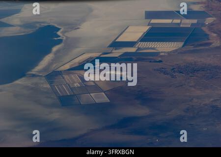 Photographie aérienne de bassins d'évaporation géométriques et d'un lac de saumure bleu profond sur les vastes plaines salées du désert, révélant des motifs industriels Banque D'Images