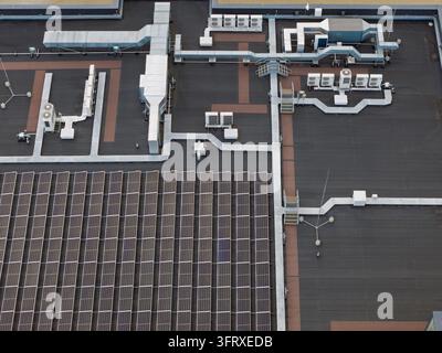 Toit d'un centre de données industriel montrant des panneaux solaires et des unités de refroidissement installées pour les systèmes de contrôle climatique pendant la journée avec des tuyaux métalliques a Banque D'Images