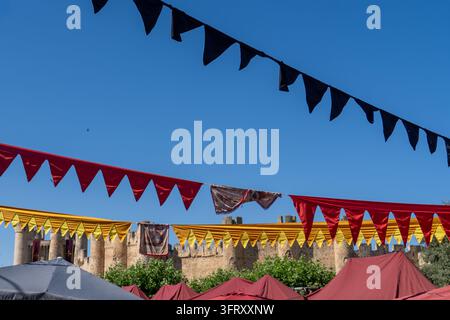 un marché ou une foire en plein air de style médiéval, décoré de fanions triangulaires colorés (rouge, jaune et noir) et de tentes à toit rouge, avec un mur de pierre Banque D'Images
