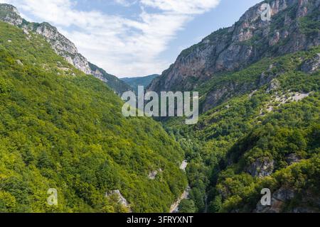 Vue aérienne du parc national de Mavrovo avec une vallée profonde, des forêts luxuriantes, des pentes montagneuses rocheuses abruptes et une route sinueuse à Mavrovo, municipalité de Banque D'Images