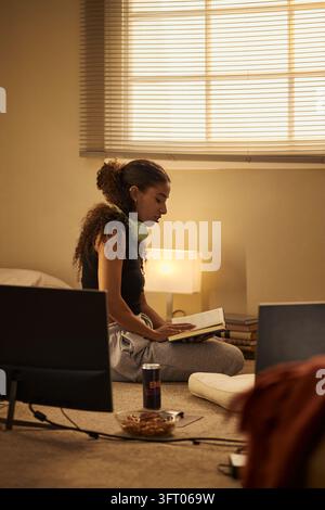 Femme biraciale lisant un livre pour l'apprentissage à distance à la maison Banque D'Images