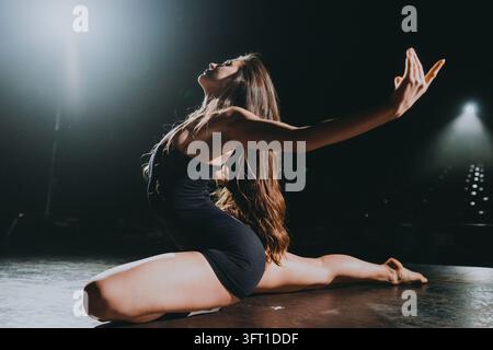 Danseuse exécutant un split expressif sur scène sous des projecteurs dramatiques, montrant force et grâce en mouvement et en forme, les longs cheveux flottant en arrière Banque D'Images