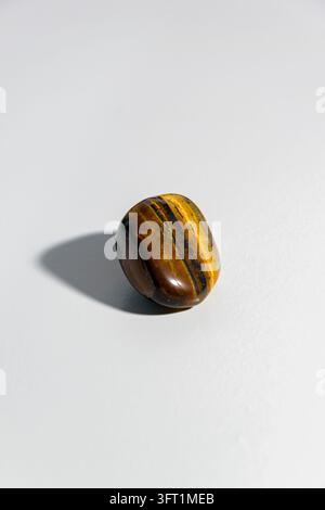 Une pierre polie couleur brun doré œil de tigre avec des bandes chatoyantes, projetant une ombre douce sur un fond blanc immaculé. Banque D'Images