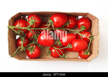Tomates rouges fraîches et mûres sur les vignes dans une boîte en carton marron pour produits. Fond alimentaire pour emballages de légumes, courses et nutrition saine. Banque D'Images