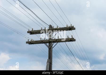 Ancien poteau utilitaire en bois avec doubles bras croisés et lignes électriques contre un ciel nuageux. Banque D'Images