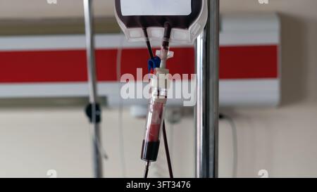 Sac de transfusion sanguine suspendu à un poteau d’infusion dans une chambre d’hôpital, avec le sang qui coule à travers la chambre à goutte dans le tube Banque D'Images