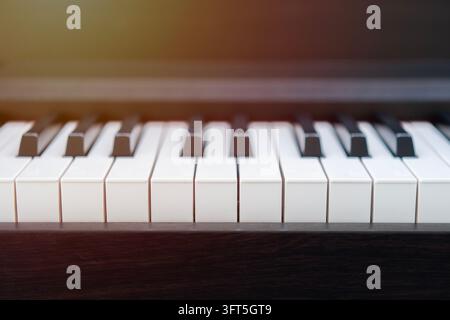 Fond de clavier de piano installé dans la salle de musique près des fenêtres le matin. Gros plan des touches du piano. Vue frontale rapprochée. Banque D'Images