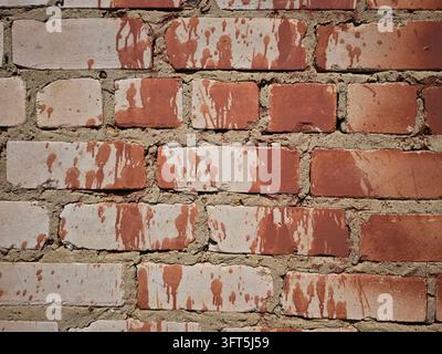 Vue rapprochée d'un mur de briques montrant des briques rouges et blanches, des éclaboussures de peinture et une texture rugueuse dans un espace urbain extérieur Banque D'Images
